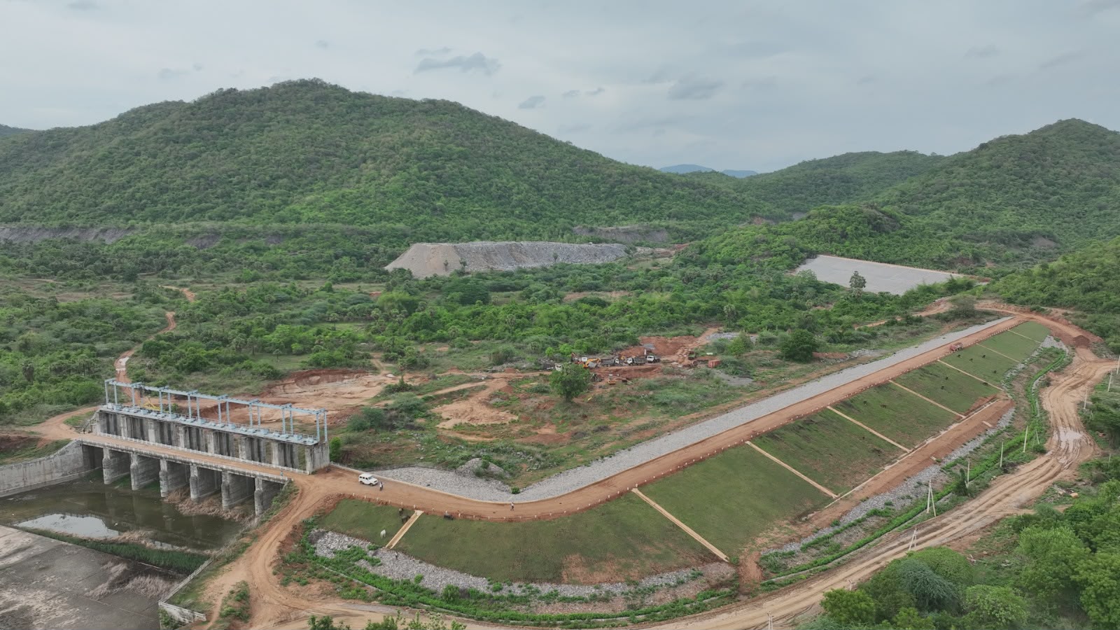 Aerial view of a barrage with gated piers and a lined canal running through green hills